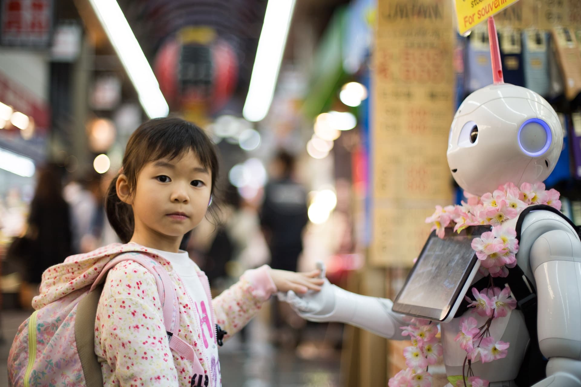 A small girl touching a hand of a humanoid robot